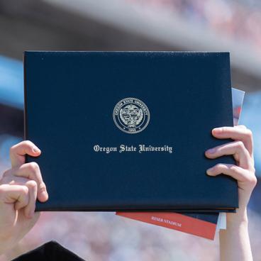 Student holds up an Oregon State University diploma.